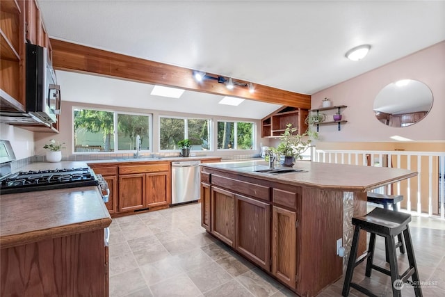 kitchen featuring sink, a kitchen breakfast bar, a kitchen island, stainless steel appliances, and vaulted ceiling with skylight