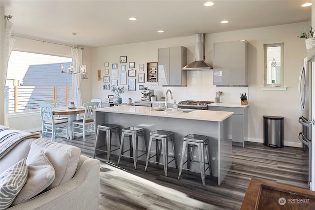 kitchen featuring gray cabinets, a breakfast bar, decorative light fixtures, sink, and wall chimney range hood