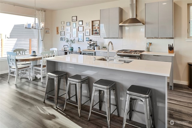 kitchen featuring wall chimney range hood, sink, gray cabinets, a breakfast bar area, and dark wood-type flooring