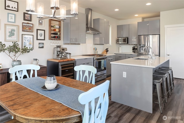 kitchen featuring stainless steel appliances, gray cabinets, wall chimney range hood, and decorative light fixtures