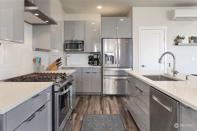 kitchen with gray cabinets, appliances with stainless steel finishes, sink, wall chimney range hood, and a wall unit AC