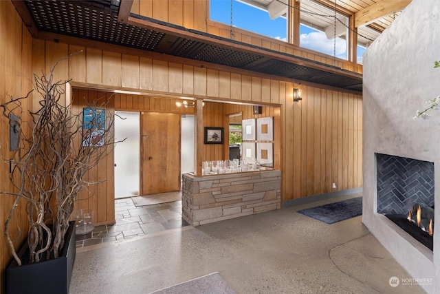 living room featuring a high ceiling, beamed ceiling, an outdoor fireplace, and wood walls