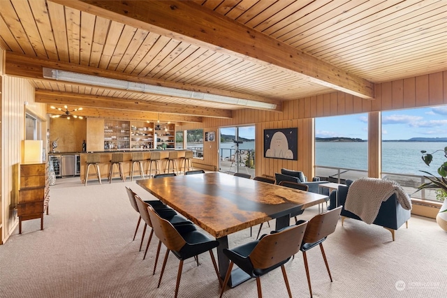 carpeted dining area featuring a water view, plenty of natural light, beam ceiling, and wood walls