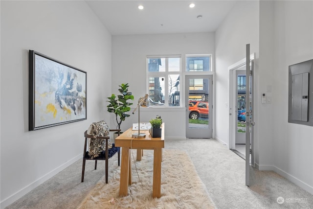 carpeted home office featuring a towering ceiling and electric panel