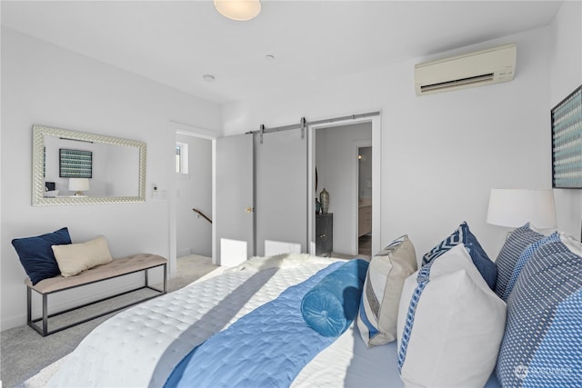 bedroom featuring connected bathroom, a barn door, a wall mounted AC, and light carpet