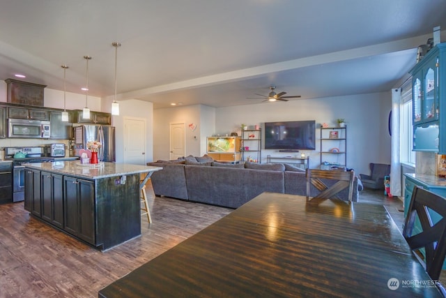 kitchen with dark brown cabinets, stainless steel appliances, light stone countertops, a kitchen island, and decorative light fixtures