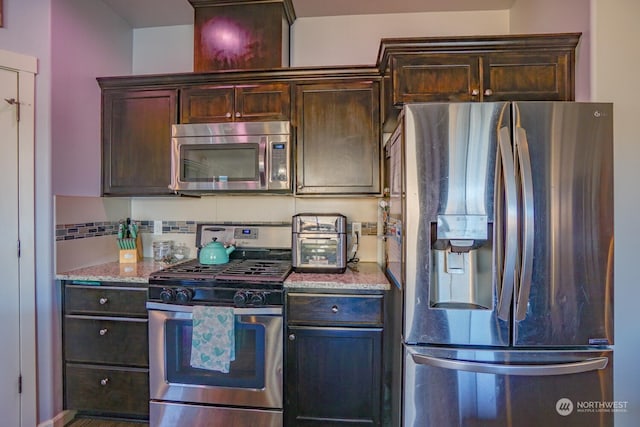 kitchen featuring dark brown cabinetry, backsplash, light stone countertops, and appliances with stainless steel finishes