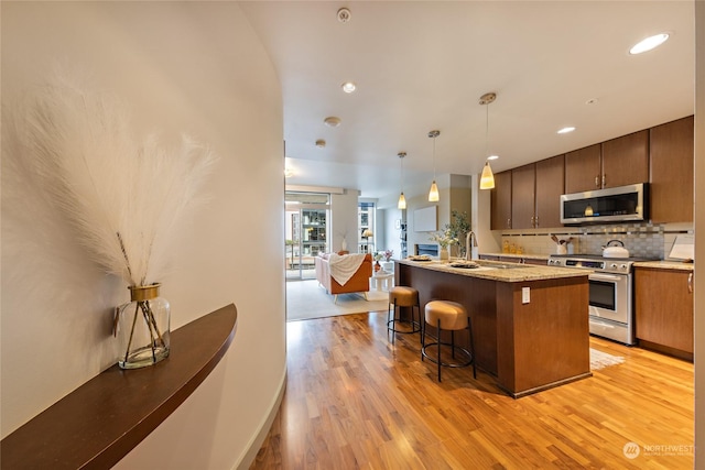 kitchen with appliances with stainless steel finishes, a kitchen breakfast bar, decorative backsplash, a center island with sink, and decorative light fixtures