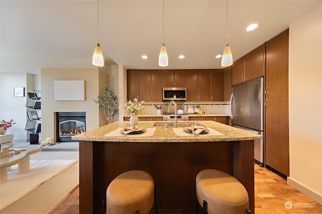 kitchen with appliances with stainless steel finishes, a kitchen bar, hanging light fixtures, and light wood-type flooring