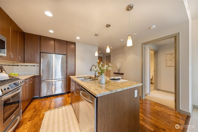 kitchen with appliances with stainless steel finishes, sink, backsplash, hanging light fixtures, and a center island with sink