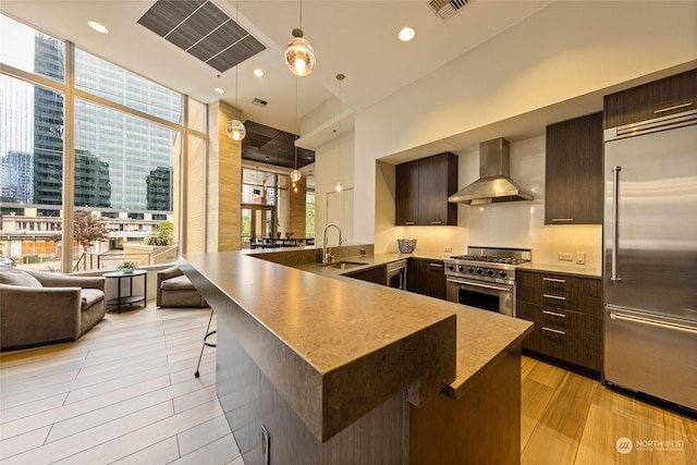 kitchen featuring wall chimney exhaust hood, sink, decorative light fixtures, light hardwood / wood-style flooring, and premium appliances