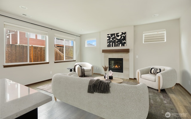 living area with a tile fireplace, baseboards, and wood finished floors