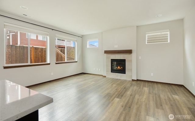 unfurnished living room featuring a tile fireplace, wood finished floors, visible vents, and baseboards