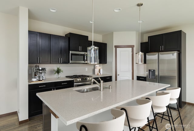 kitchen with stainless steel appliances, a breakfast bar, a sink, decorative backsplash, and dark wood-style floors