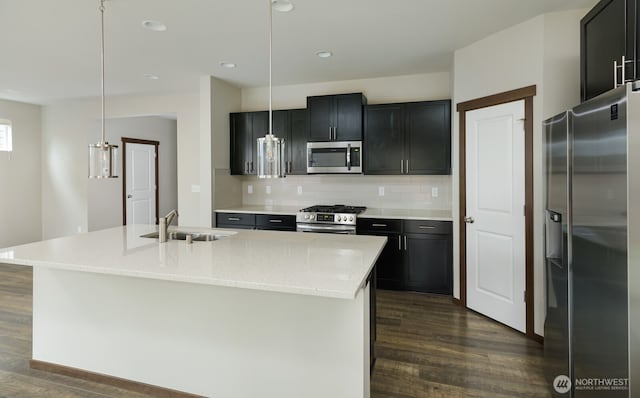 kitchen featuring dark cabinets, stainless steel appliances, a sink, backsplash, and dark wood finished floors