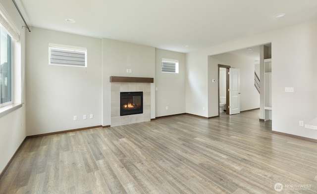 unfurnished living room with a tiled fireplace, wood finished floors, and baseboards