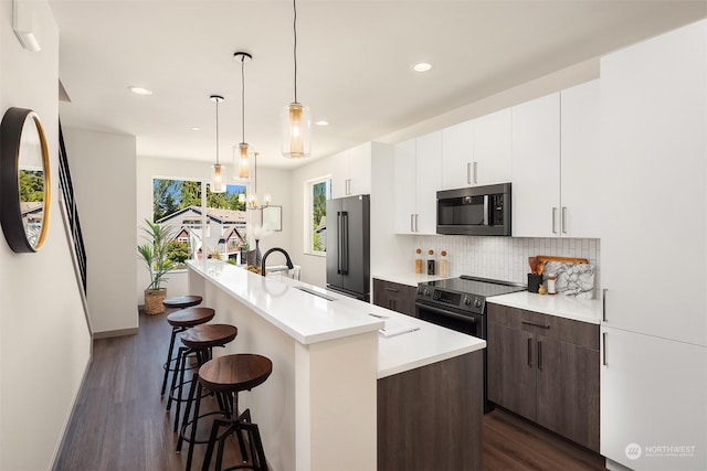 kitchen with appliances with stainless steel finishes, tasteful backsplash, white cabinetry, a kitchen island with sink, and dark brown cabinetry