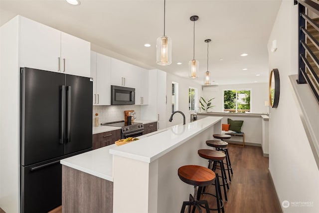 kitchen featuring a breakfast bar, black fridge, decorative light fixtures, electric stove, and a kitchen island with sink