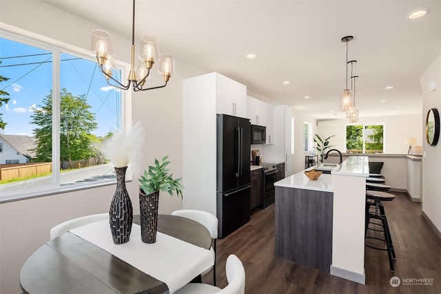 kitchen with pendant lighting, sink, white cabinetry, black appliances, and an island with sink