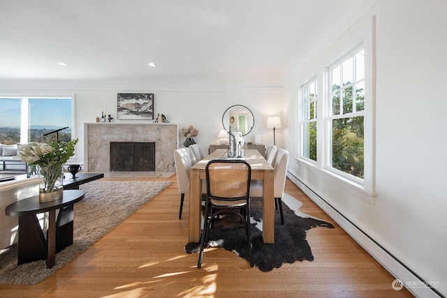 dining room featuring crown molding, a baseboard radiator, a high end fireplace, and light hardwood / wood-style flooring