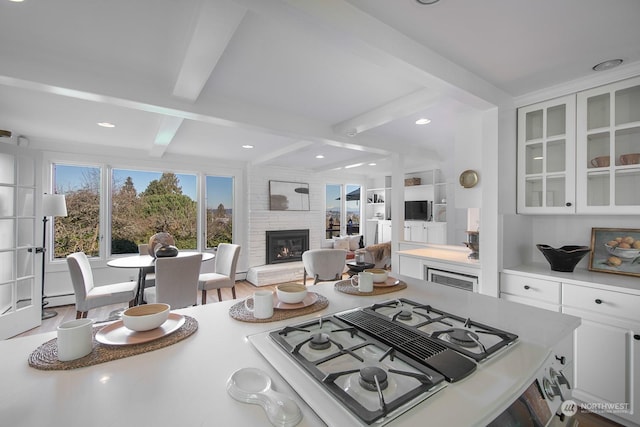 kitchen featuring beam ceiling, gas cooktop, a fireplace, hardwood / wood-style floors, and white cabinets