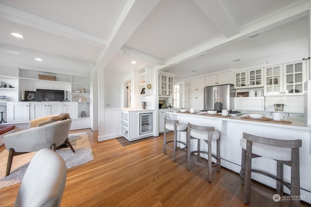 kitchen featuring light hardwood / wood-style flooring, stainless steel refrigerator, white cabinetry, beam ceiling, and kitchen peninsula