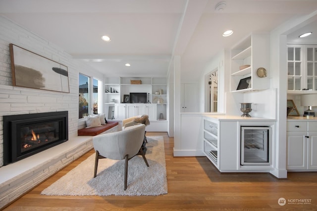 bar featuring a stone fireplace, light wood-type flooring, built in features, beamed ceiling, and white cabinets