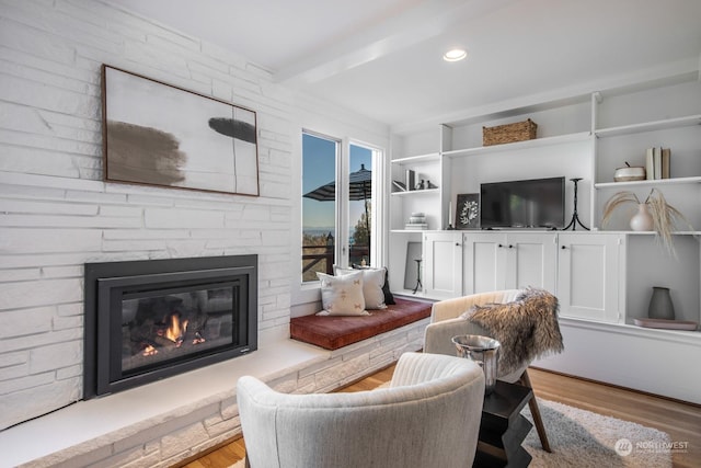 living room featuring beam ceiling, a fireplace, and light hardwood / wood-style floors