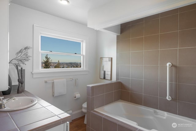 bathroom featuring vanity, tiled bath, and toilet