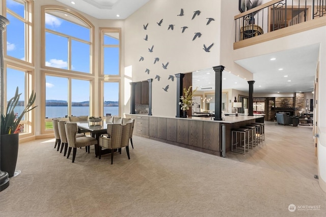 dining area with a high ceiling, a water view, light carpet, and decorative columns