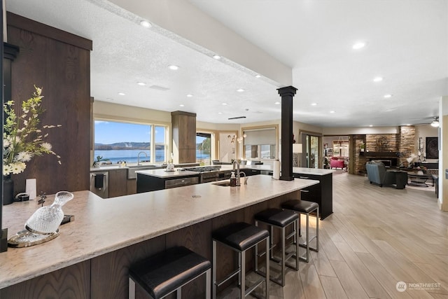 kitchen with light hardwood / wood-style flooring, a water view, a textured ceiling, a kitchen bar, and ornate columns