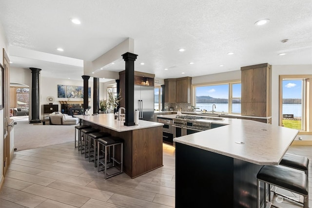 kitchen with appliances with stainless steel finishes, decorative columns, a breakfast bar area, a kitchen island with sink, and a water view