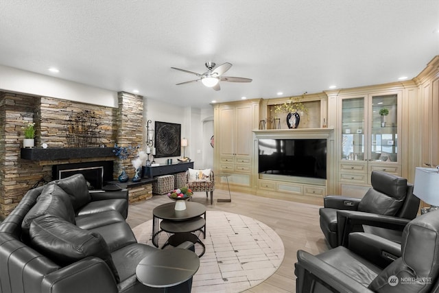 living room featuring ceiling fan, a fireplace, light hardwood / wood-style floors, and a textured ceiling