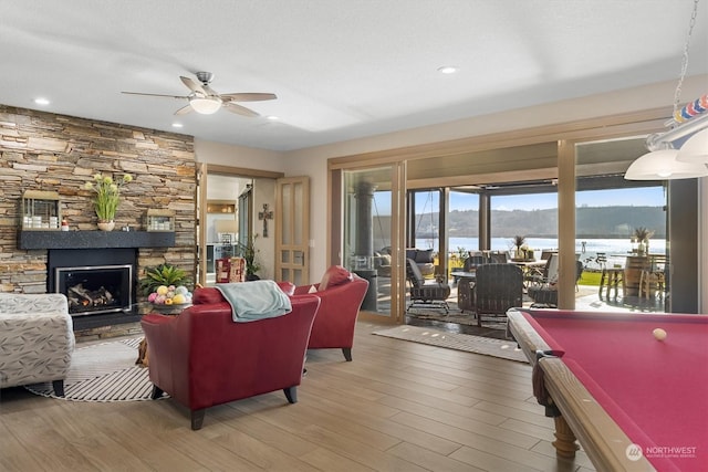 living room featuring a water view, pool table, hardwood / wood-style flooring, ceiling fan, and a fireplace