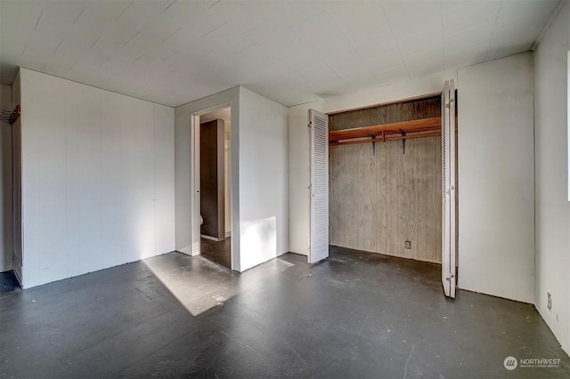 unfurnished bedroom with a closet and wood walls