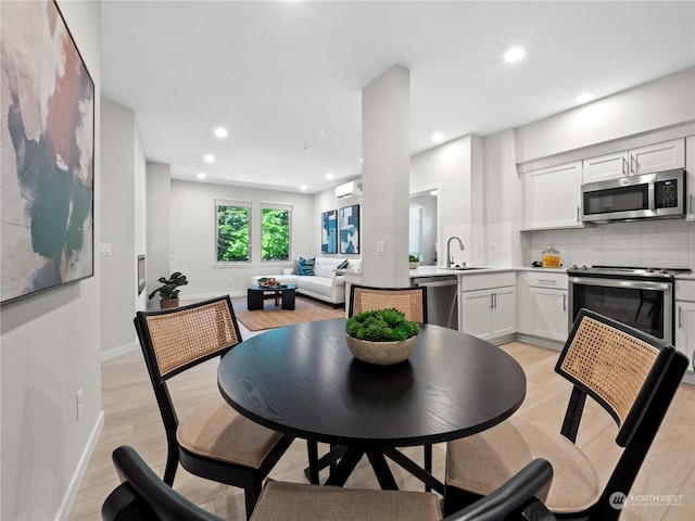 dining area featuring sink, a wall unit AC, and light wood-type flooring