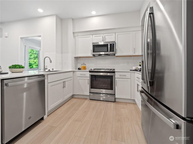 kitchen featuring stainless steel appliances, white cabinetry, tasteful backsplash, and light hardwood / wood-style floors