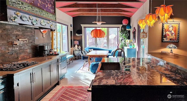 kitchen with pendant lighting, ventilation hood, sink, stainless steel gas cooktop, and a center island with sink