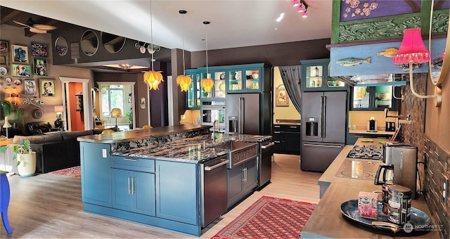 kitchen with appliances with stainless steel finishes, a kitchen island with sink, pendant lighting, and light wood-type flooring