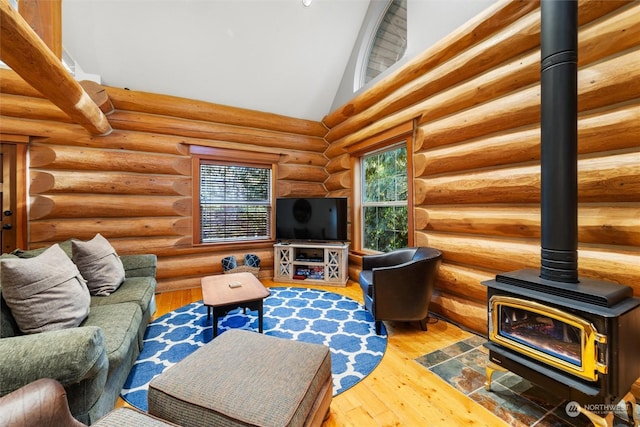 living room featuring wood-type flooring, rustic walls, high vaulted ceiling, and a wood stove