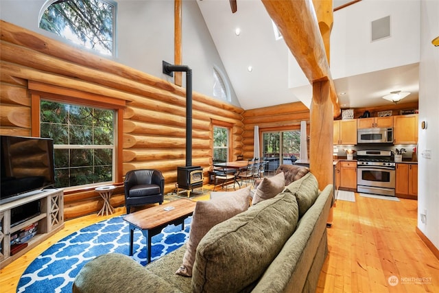 living room with log walls, a wealth of natural light, high vaulted ceiling, and a wood stove