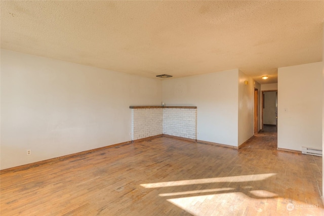 empty room with baseboard heating, wood-type flooring, and a textured ceiling