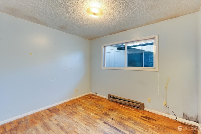 empty room featuring hardwood / wood-style floors, a baseboard radiator, and a textured ceiling