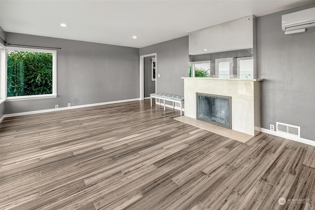 unfurnished living room featuring wood-type flooring, plenty of natural light, and a wall unit AC