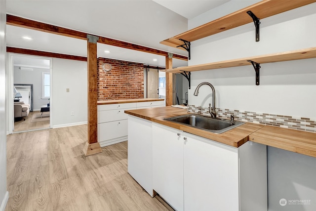 kitchen with butcher block counters, sink, white cabinetry, brick wall, and decorative backsplash