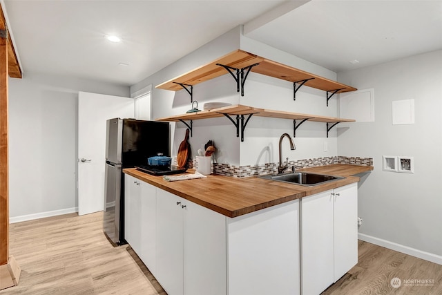 kitchen with white cabinetry, butcher block countertops, sink, and light wood-type flooring