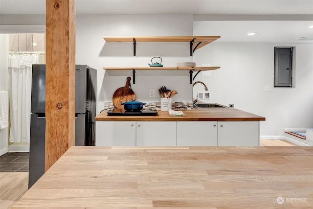 bar featuring sink, stainless steel fridge, electric panel, white cabinets, and light wood-type flooring