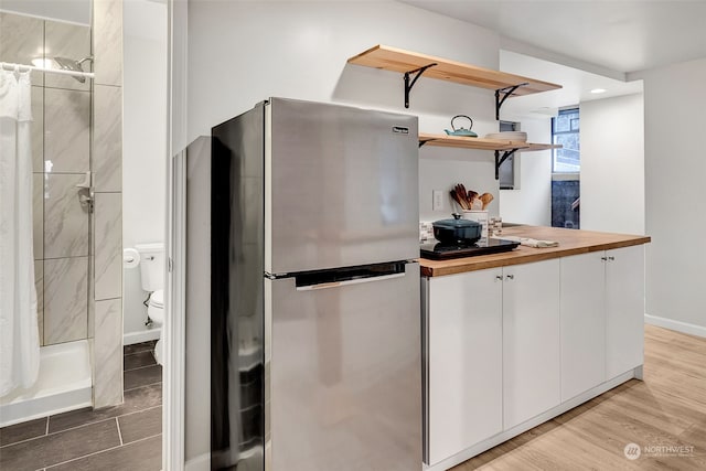 kitchen with light hardwood / wood-style flooring, stainless steel fridge, wooden counters, and white cabinets