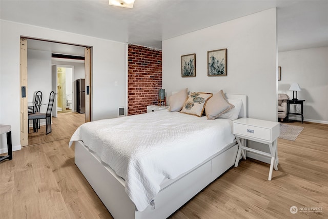 bedroom featuring stainless steel fridge and light hardwood / wood-style floors