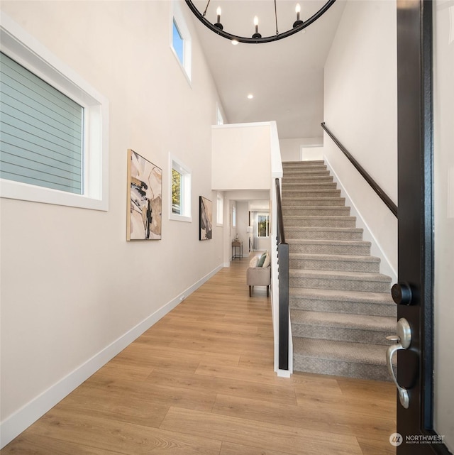 foyer entrance featuring an inviting chandelier, a towering ceiling, a healthy amount of sunlight, and light hardwood / wood-style flooring